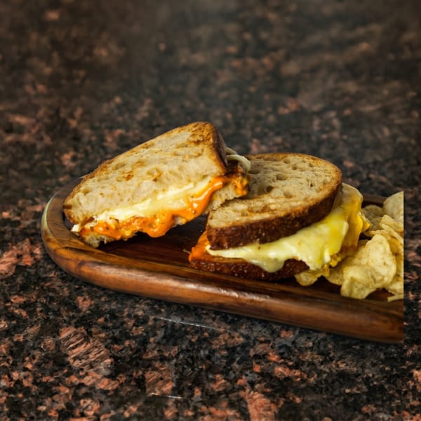 Two halves of a grilled cheese sandwich with melted orange and white cheese, served with chips.