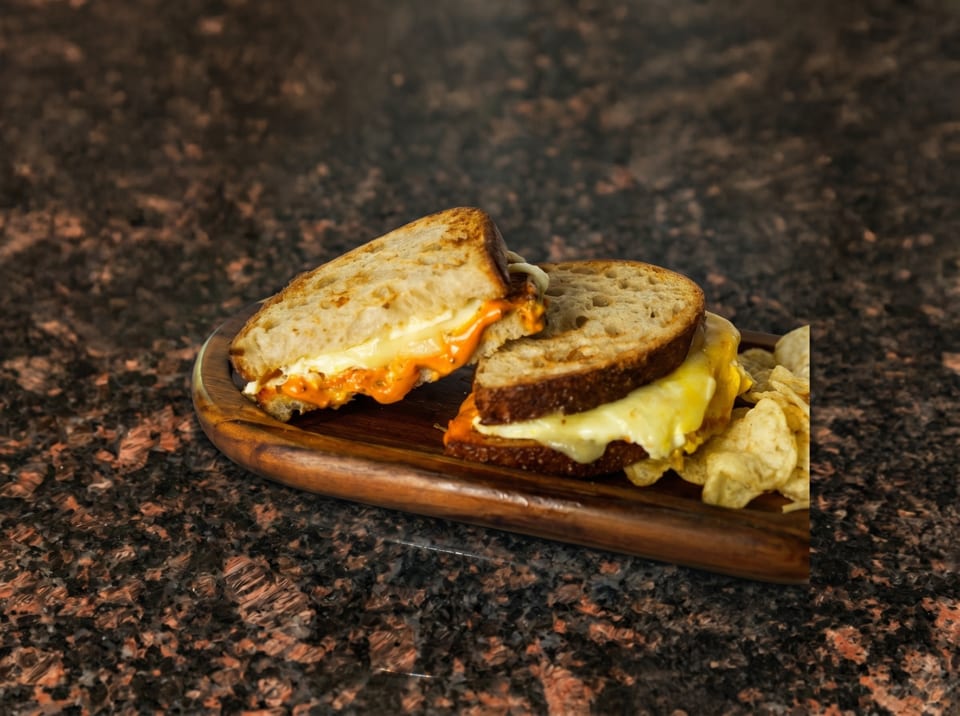 Two halves of a grilled cheese sandwich with melted orange and white cheese, served with chips.