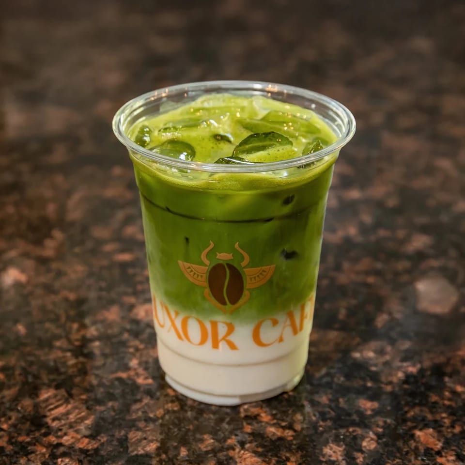 Iced matcha latte with a Luxor Cafe logo on a dark speckled counter.