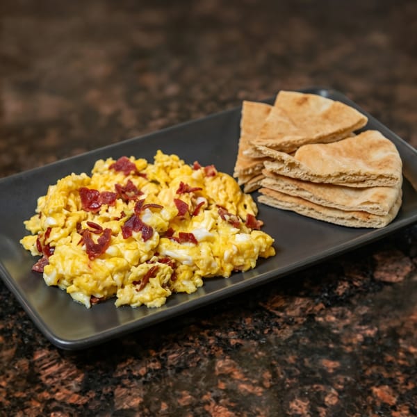 Scrambled eggs with bacon bits and pita bread on a black rectangular plate.