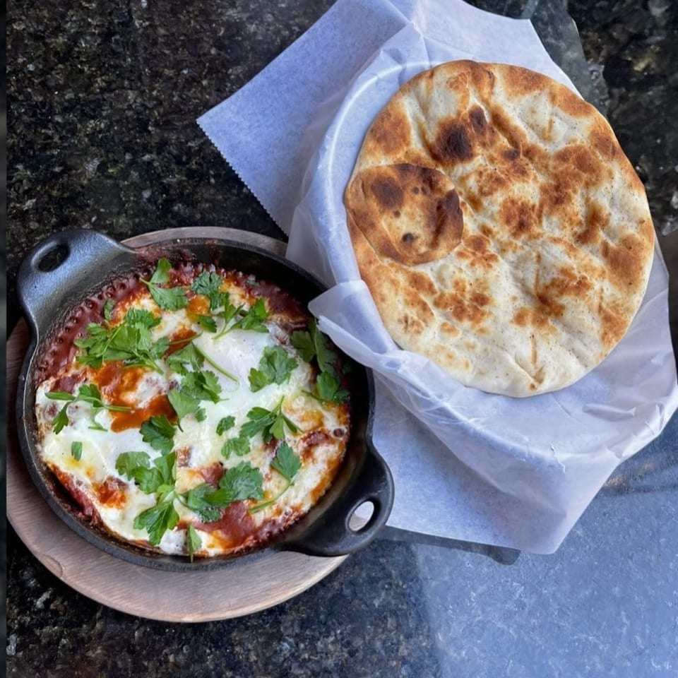 Shakshuka in a cast iron skillet with fresh parsley, served with warm pita bread.