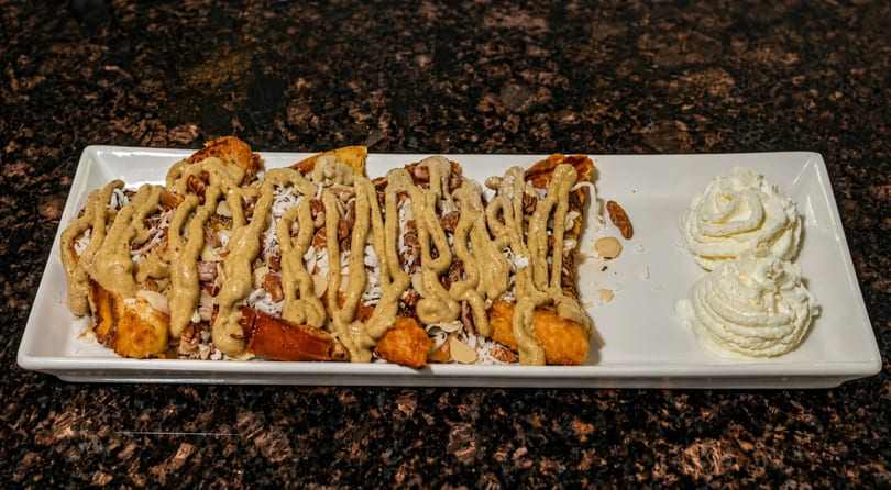 French toast sticks drizzled with sauce, nuts, and shredded coconut, served with whipped cream.