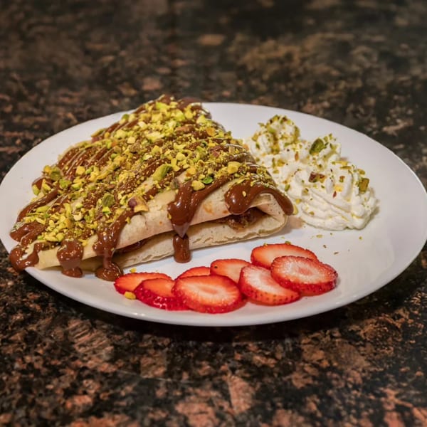 Crepe drizzled with chocolate and pistachios, served with whipped cream and sliced strawberries.