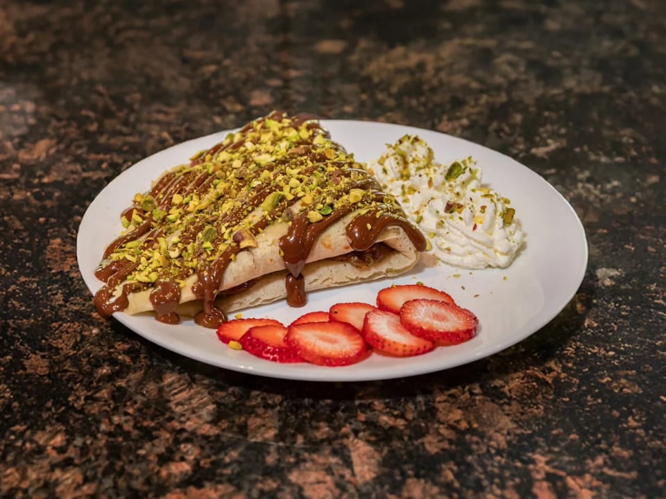 Crepe drizzled with chocolate and pistachios, served with whipped cream and sliced strawberries.